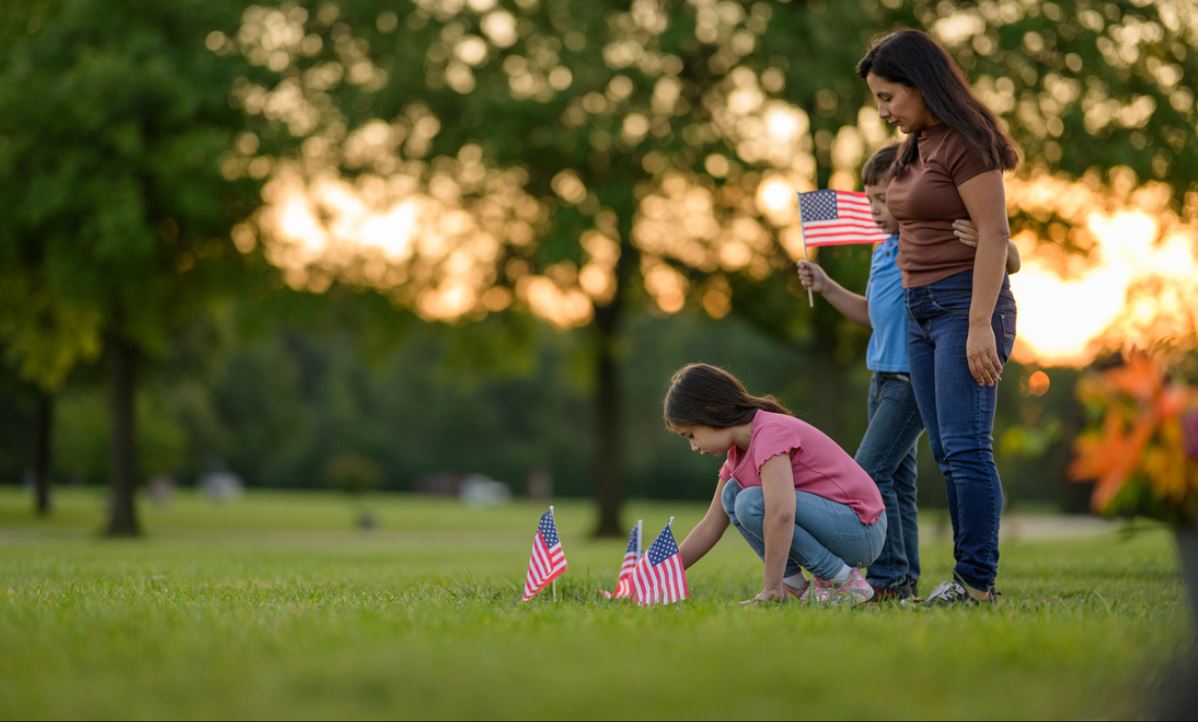 A mother and two young children in a cemetery with small American flags