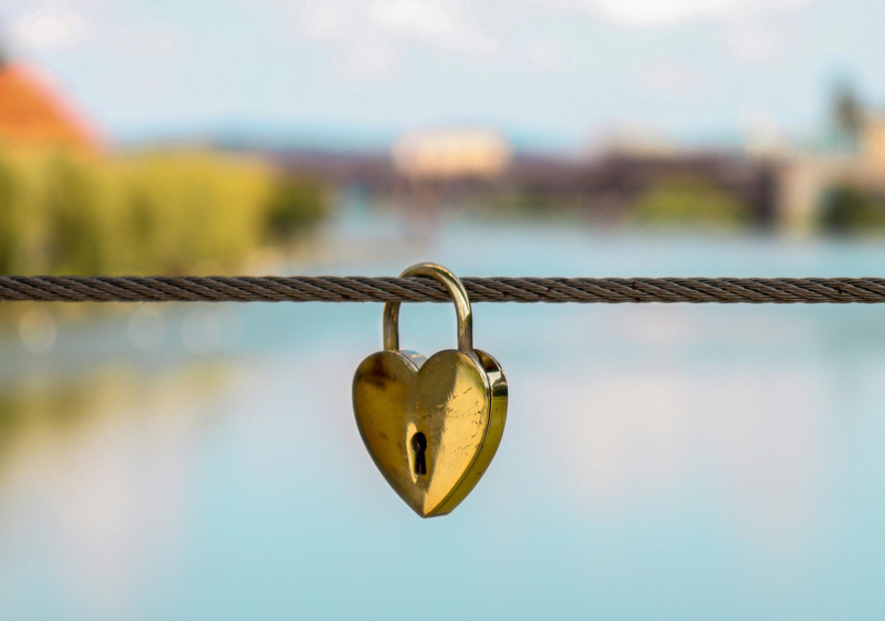 A heart shaped lock hangs from a fence on a bridge