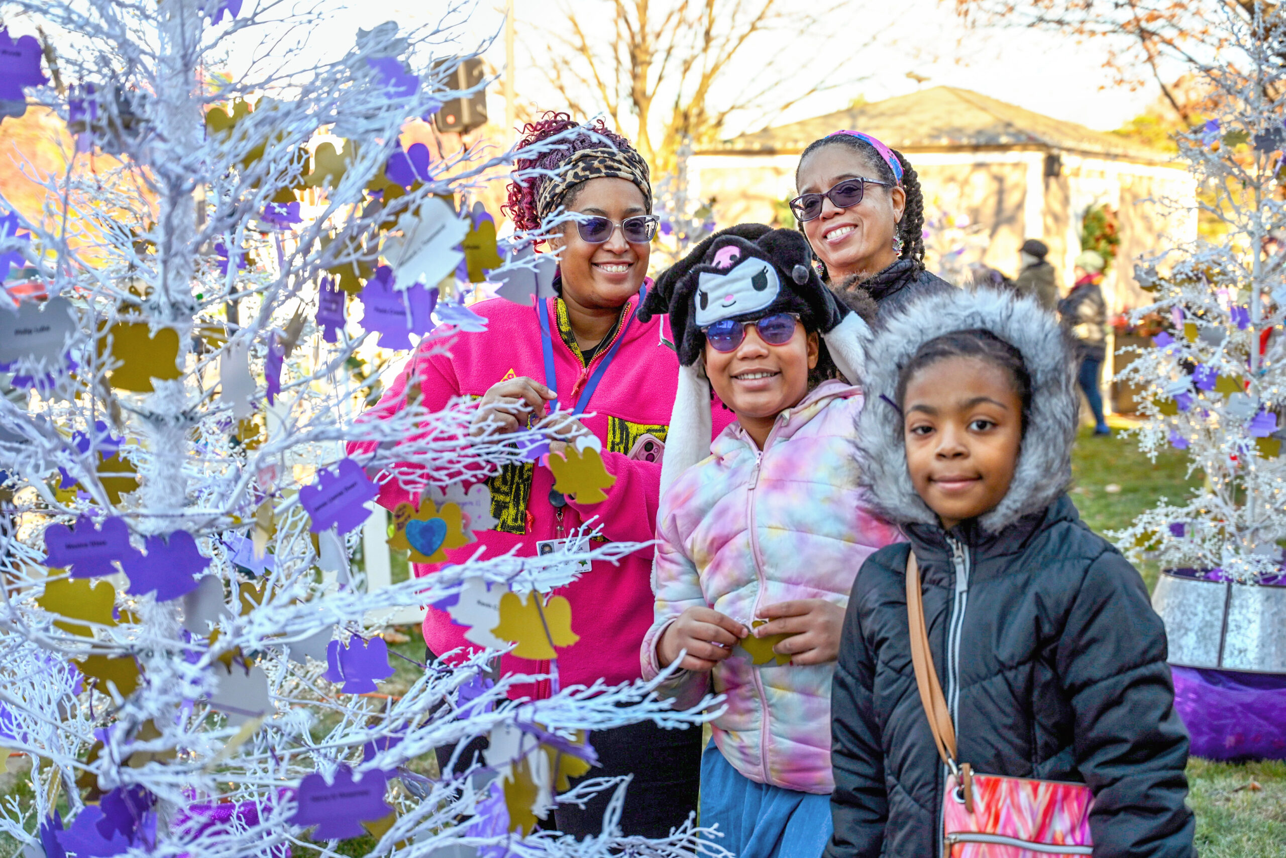 A family including a mother and adult daughter with two little girls are outside hanging angel ornaments on a Christmas tree.