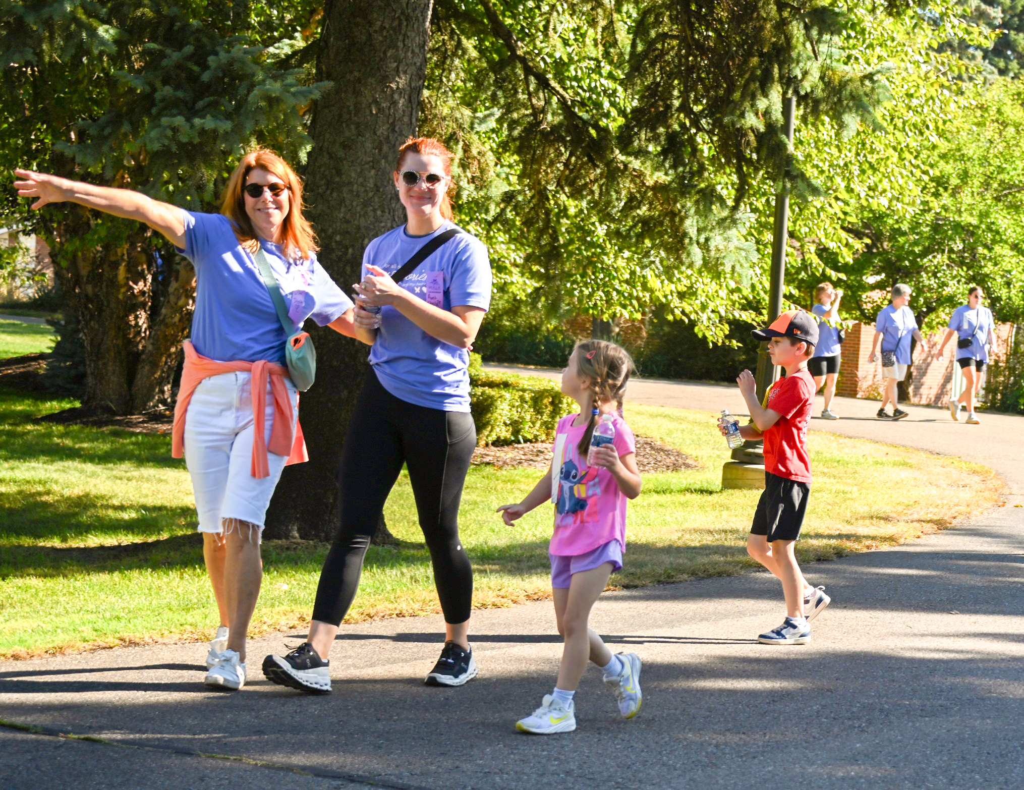 adults and children walking on a sunny day on a tree-lined path