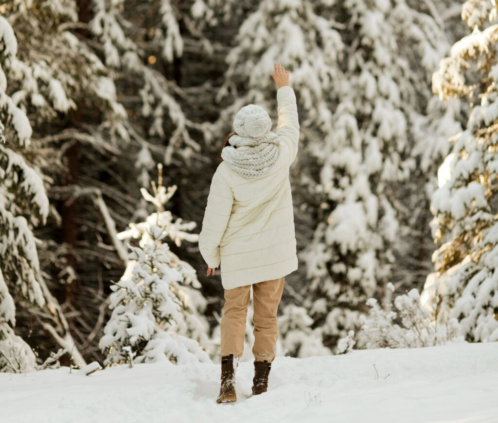 a woman in a winter coat walks through a snowy landscape with her hand stretched toward the sky