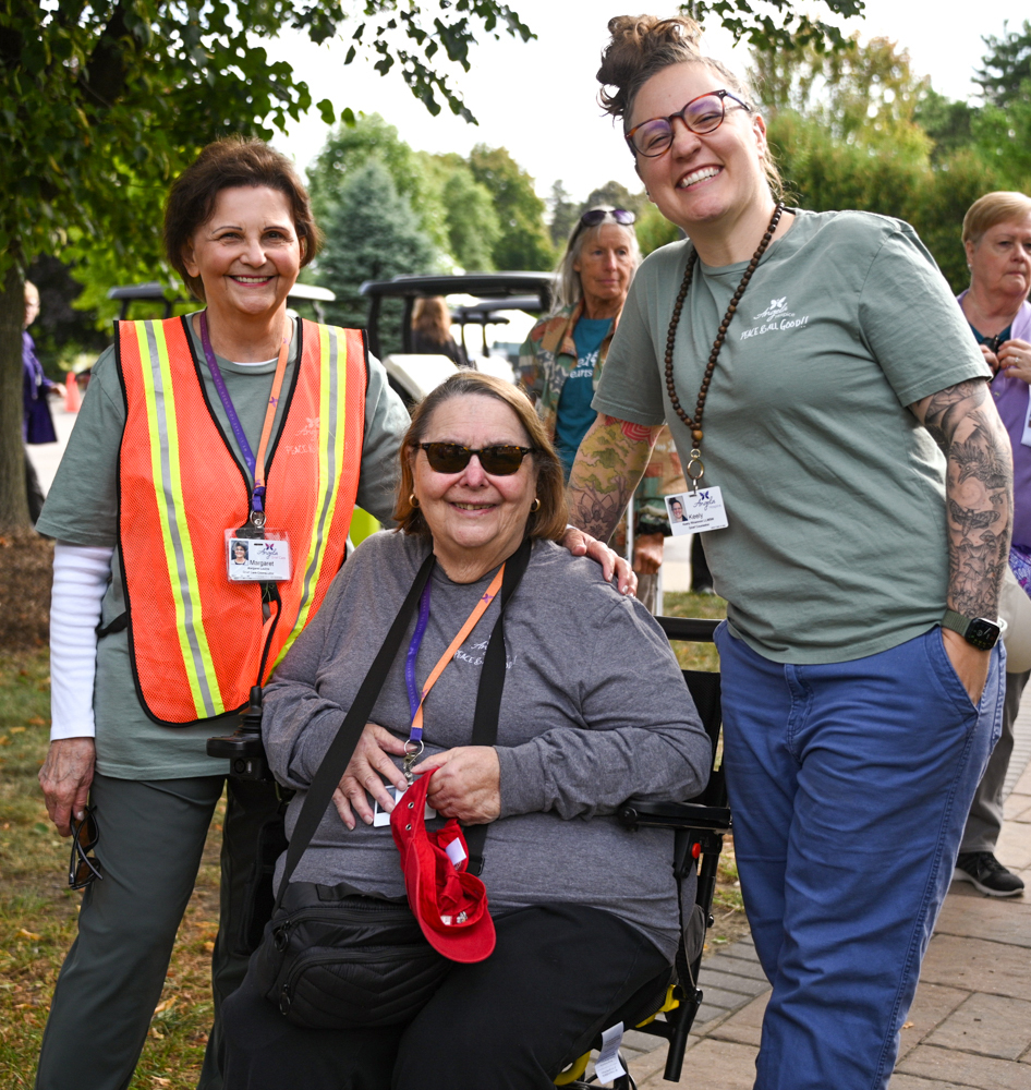 A group of smiling people outdoors, two standing and one seated, wearing ID badges and casual clothes.